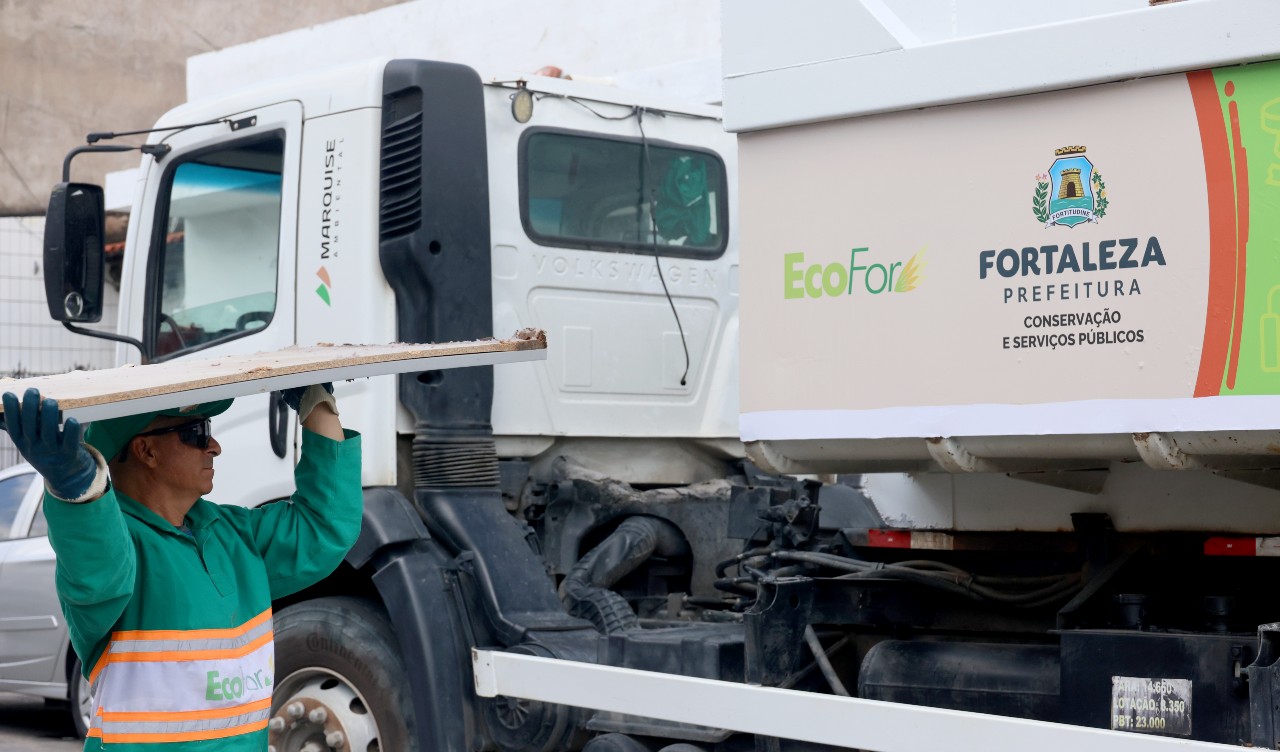 homem colocando um pedaço de madeira num caminhão limpezinha